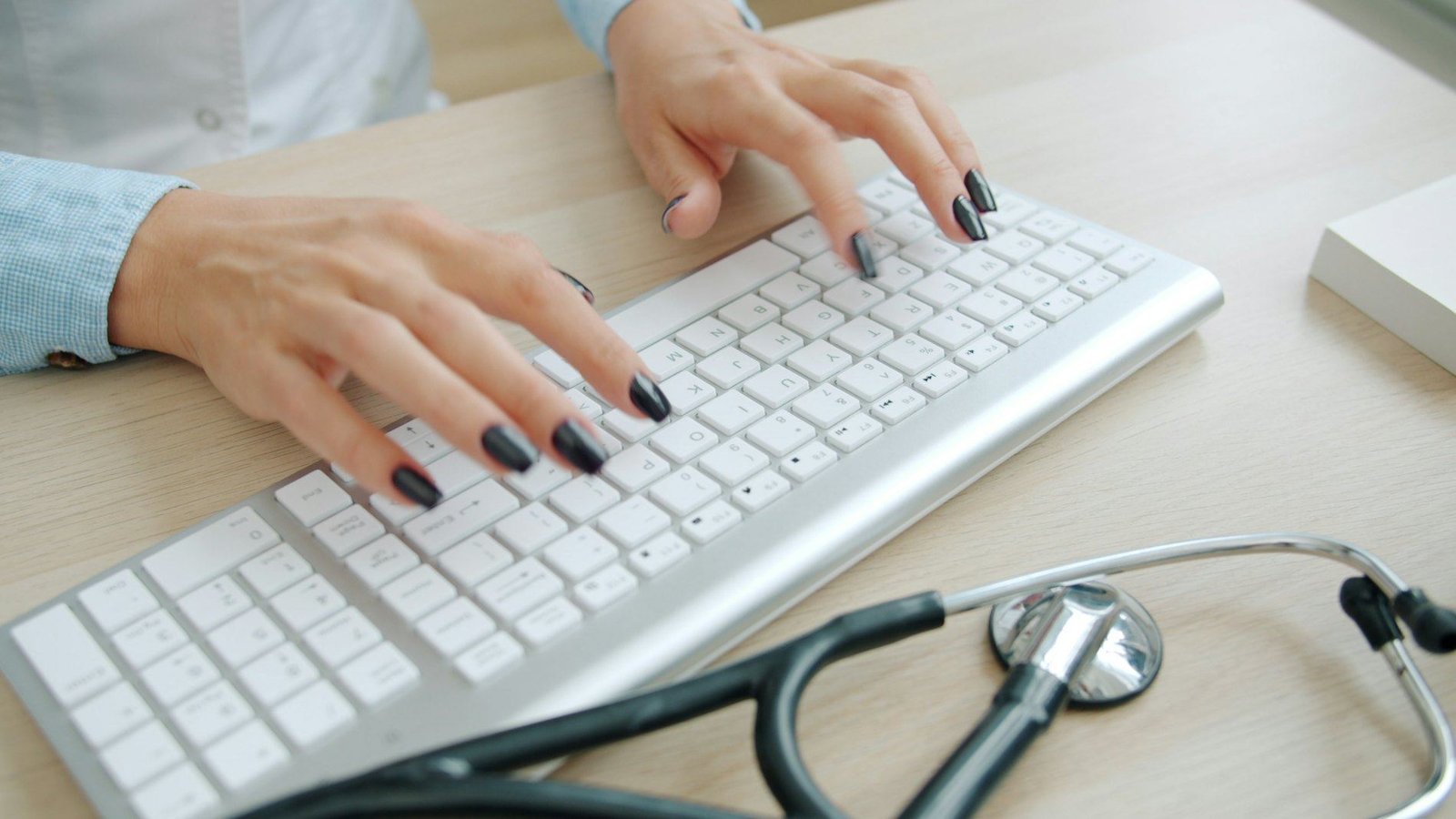 Doctor typing at a desk with a stethoscope nearby
