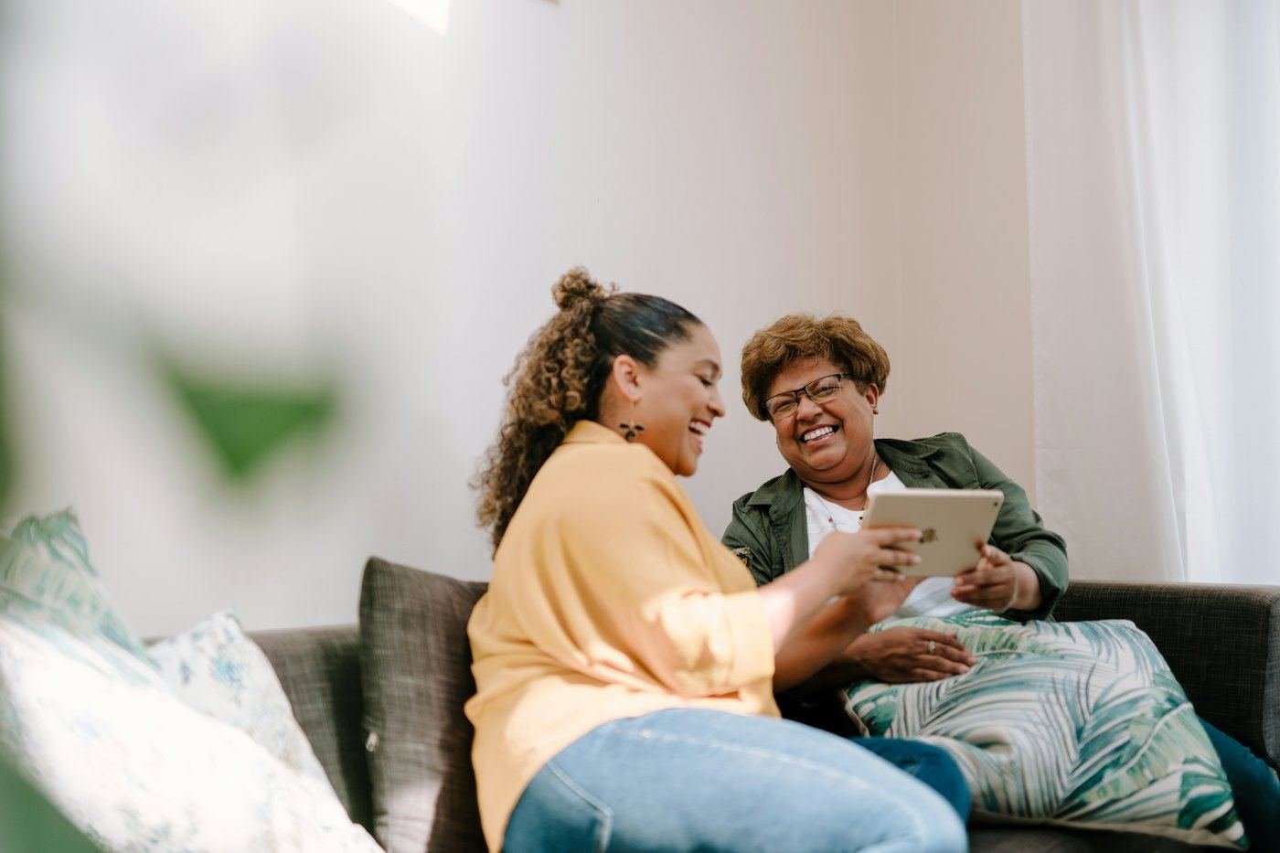 Adult daughter and her mother looking at a tablet together on the sofa